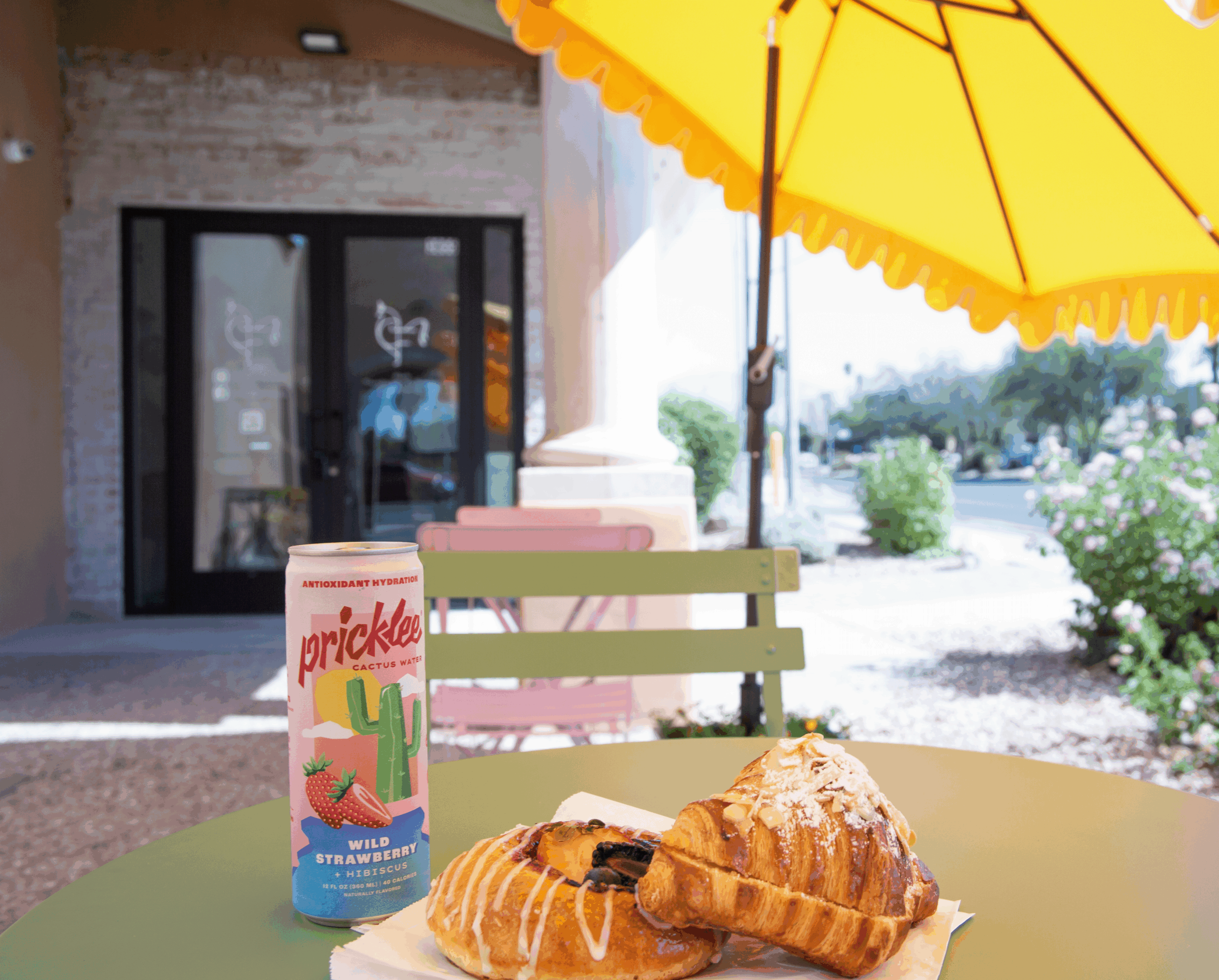 Pastries and a can of Pricklee cactus water on an outdoor café table under a yellow umbrella